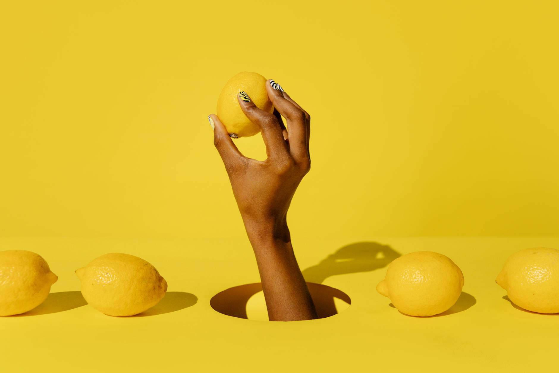 Mano che tiene un limone fresco su sfondo giallo vibrante, simbolo di sensibilità e rinnovamento