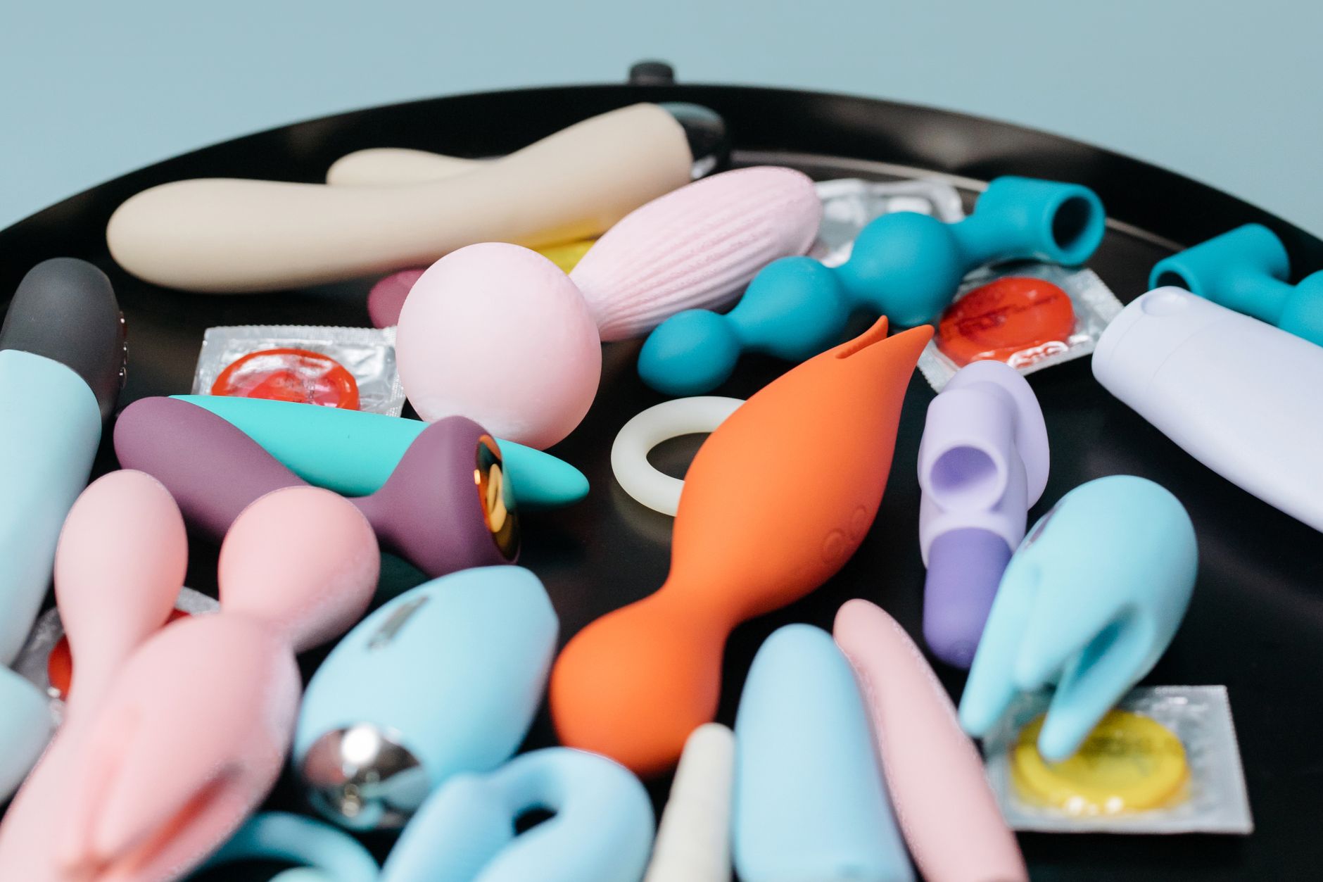 Donna con occhiali che tiene vibratori in silicone blu e rosa in atteggiamento contemplativo