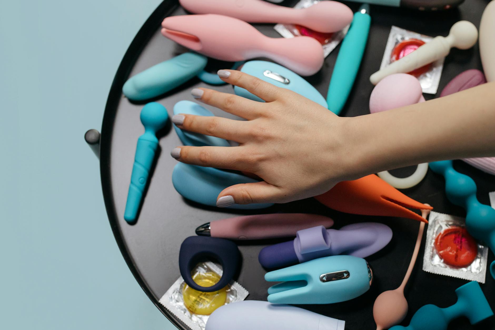 Una mano che raggiunge una varietà di vibratori colorati disposti su un tavolo.