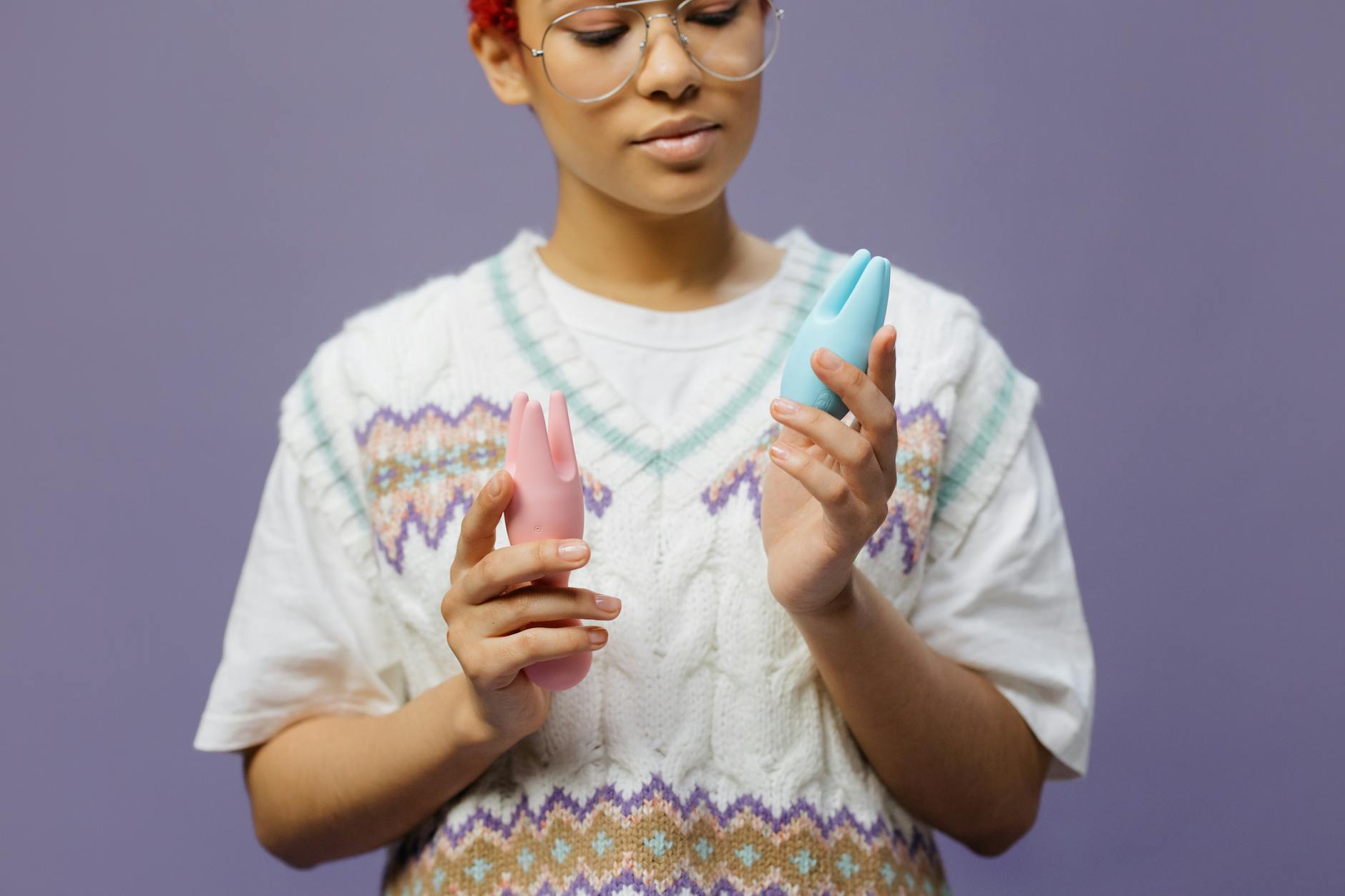 Una donna con occhiali tiene in mano delicati vibratori colorati in silicone, con uno sguardo consapevole e contemplativo.